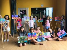 a group of children holding up paintings in front of their faces and posing for the camera