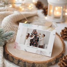 a christmas card sitting on top of a wooden slice next to pine cones and candles