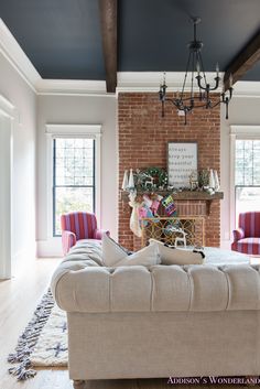 the living room is decorated in white and red with striped chairs, a chandelier, and a brick fireplace