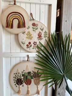 three hand embroidered wall hangings on a white door with a palm tree in the foreground