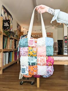 a person holding a bag made out of quilts in a room with bookshelves