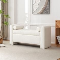 a living room with white furniture and a plant in the corner on the rugs