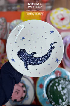 a person holding up a plate with a whale on it in front of other plates