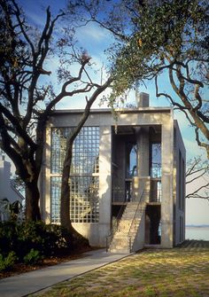 an unusual house sits on the edge of a grassy area with trees and water in the background