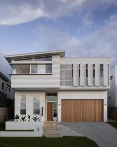 a modern house with white siding and wood accents on the front door is shown at dusk