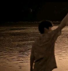 a man flying a kite on the beach at night with his arms in the air