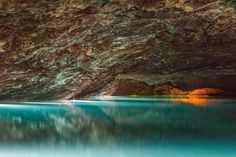 the water is very blue and green in this cave with red rocks on it's sides