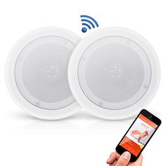 two white speakers are being held up by a person's hand with an iphone in front of them