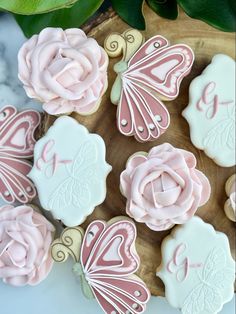 decorated cookies with pink icing and butterflies on a wooden platter next to green leaves