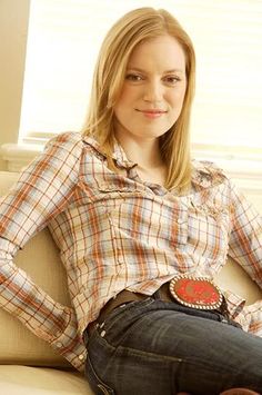 a young woman sitting on top of a couch wearing a plaid shirt and jean pants