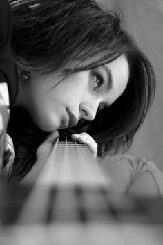 a woman is playing the guitar with her head on her hand and looking at the camera