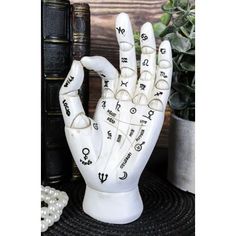 a white ceramic hand with numbers and symbols on it, next to some books in front of a potted plant