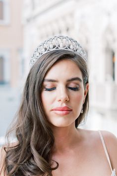 a woman wearing a tiara and looking down at her face while standing in front of a building