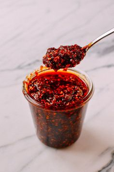 a spoon full of red sauce on top of a glass jar filled with something else