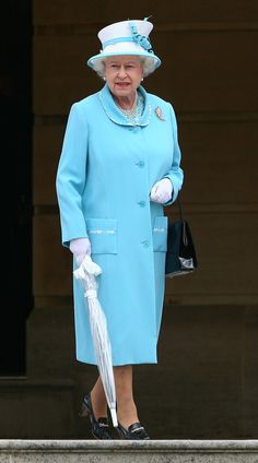 an older woman in a blue coat and hat holding an umbrella on the steps of buckingham palace