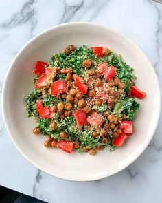 a white bowl filled with lots of food on top of a marble countertop next to a knife and fork