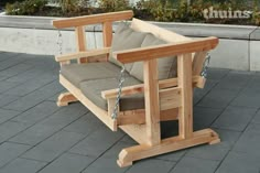 a wooden swing chair sitting on top of a brick floor next to a planter