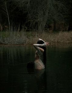 a woman standing in the water with her back turned to the camera and arms outstretched