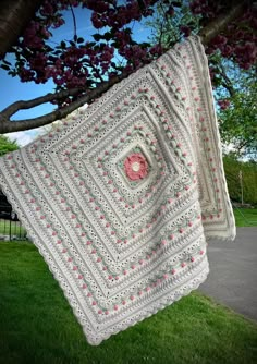 two crocheted afghans hanging from a tree in front of some grass and flowers