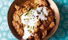 a bowl filled with meat covered in white sauce and garnished with pistachio seeds