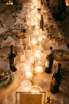 a long table is set with wine glasses and plates, candles in front of them