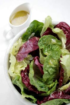 a bowl filled with lettuce next to a cup of dressing