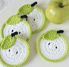 four crocheted apples are on a plate next to an apple