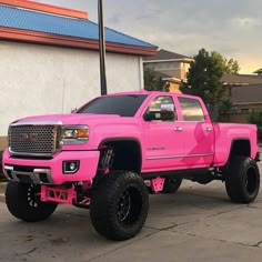 a bright pink truck parked in front of a building with black tires and rims