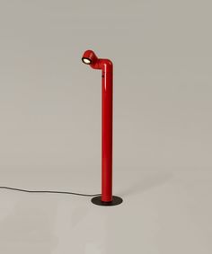 a red floor lamp sitting on top of a white table next to a light bulb