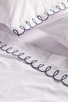 an unmade bed with white sheets and black writing on the pillowcase, along with two pillows