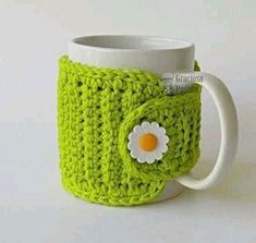 a green crocheted coffee cup with a white flower on the front and side