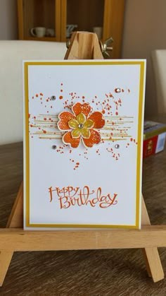 a happy birthday card sitting on top of a wooden easel with an orange flower