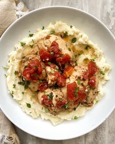 a white bowl filled with mashed potatoes and meat covered in tomatoes, garnished with parsley