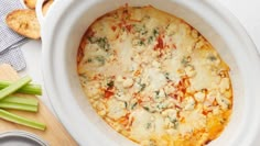 a casserole dish with cheese and vegetables on a wooden cutting board next to crackers