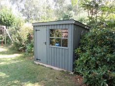 a small gray shed sitting in the middle of a yard next to bushes and trees