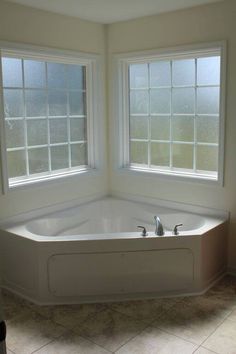 a large white bath tub sitting next to two windows in a room with tile flooring