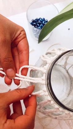 two hands are tying rope to a glass jar with blue beads on the top and bottom