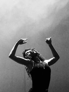 a black and white photo of a woman with her arms in the air, looking up