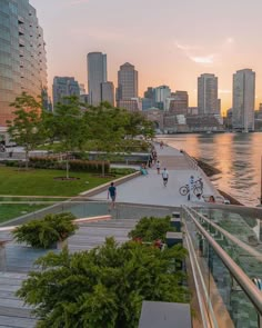 people are walking along the boardwalk in front of some tall buildings and water at sunset