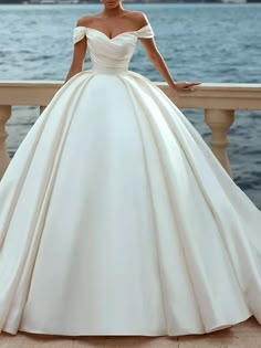 a woman in a white wedding dress standing on a balcony near the water with her hands on her hips