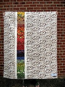 a person standing in front of a brick wall holding up a quilt