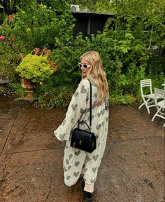 a woman standing in the rain with her hand on her hip bag and wearing sunglasses