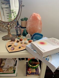 a white table topped with lots of books and other items next to a large mirror