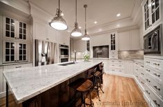 a large kitchen with white cabinets and marble counter tops, along with wooden flooring