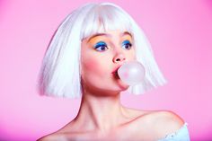 a woman with white hair and blue eyes is blowing a bubble into her mouth while wearing a white wig