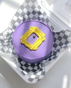 a purple and yellow cake sitting on top of a checkered paper plate in a box