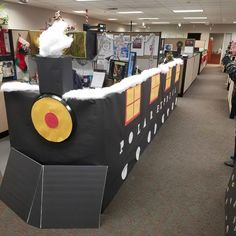 an office decorated for christmas with a train on the wall and people looking at it