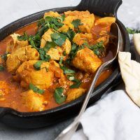 a pan filled with curry and chicken on top of a table next to pita bread