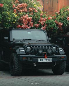 a black jeep is parked in front of some pink flowers