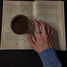 a person is holding a cup of coffee in their hand and reading a book with an open page